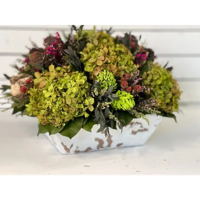 About this product The Diana is one of our newest signature pieces. Shown in Preserved basil hydrangea blooms coupled with preserved heather, tortum, Phylicia, greenery, magnolia and Concho pods make for a gorgeous and timeless floral arrangement. It will brighten up your home and bring life to your space whatever the season. The container is a white square wood bowl. No maintenance required. Also, comes in Natural Hydrangea. Approximately 15" x 15" x 9 to 10" Tall Details • Made in United States